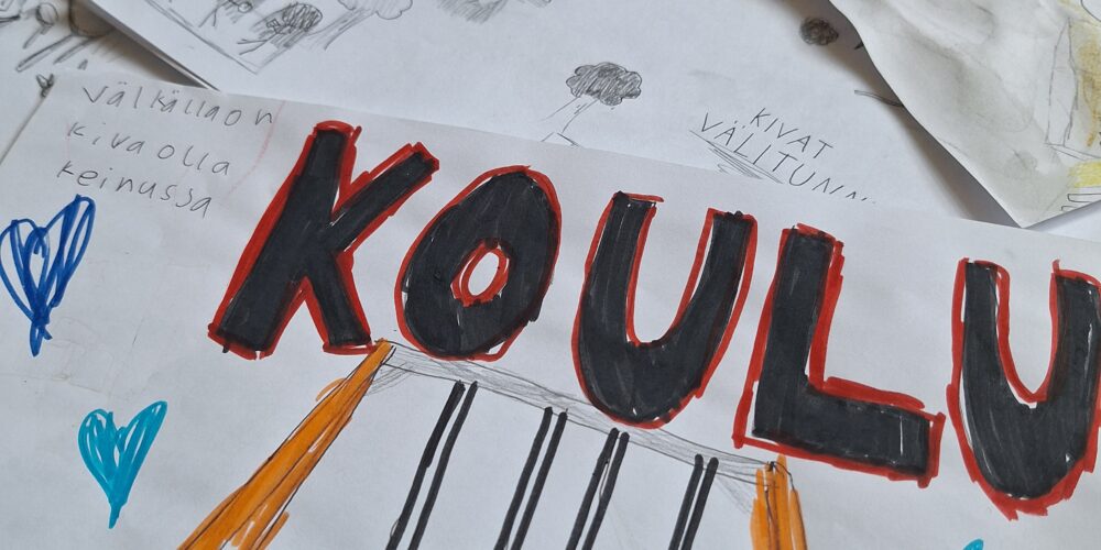 Lähikuva lasten piirtämistä värikkäistä piirustuksista, joita on pinossa päällekkäin. Päällimmäisessä piirustuksessa on teksti ”KOULU”, kaksi lasta keinumassa sekä erivärisiä sydämiä. Piirustuksen reunassa lukee: ”Välkällä on kiva olla keinussa”. Taustalla näkyy muita piirustuksia, joissa on kuvattu muun muassa kavereita ja puita sekä tekstejä kuten ”kivat välitunnit” ja ”hyvä työrauha”.